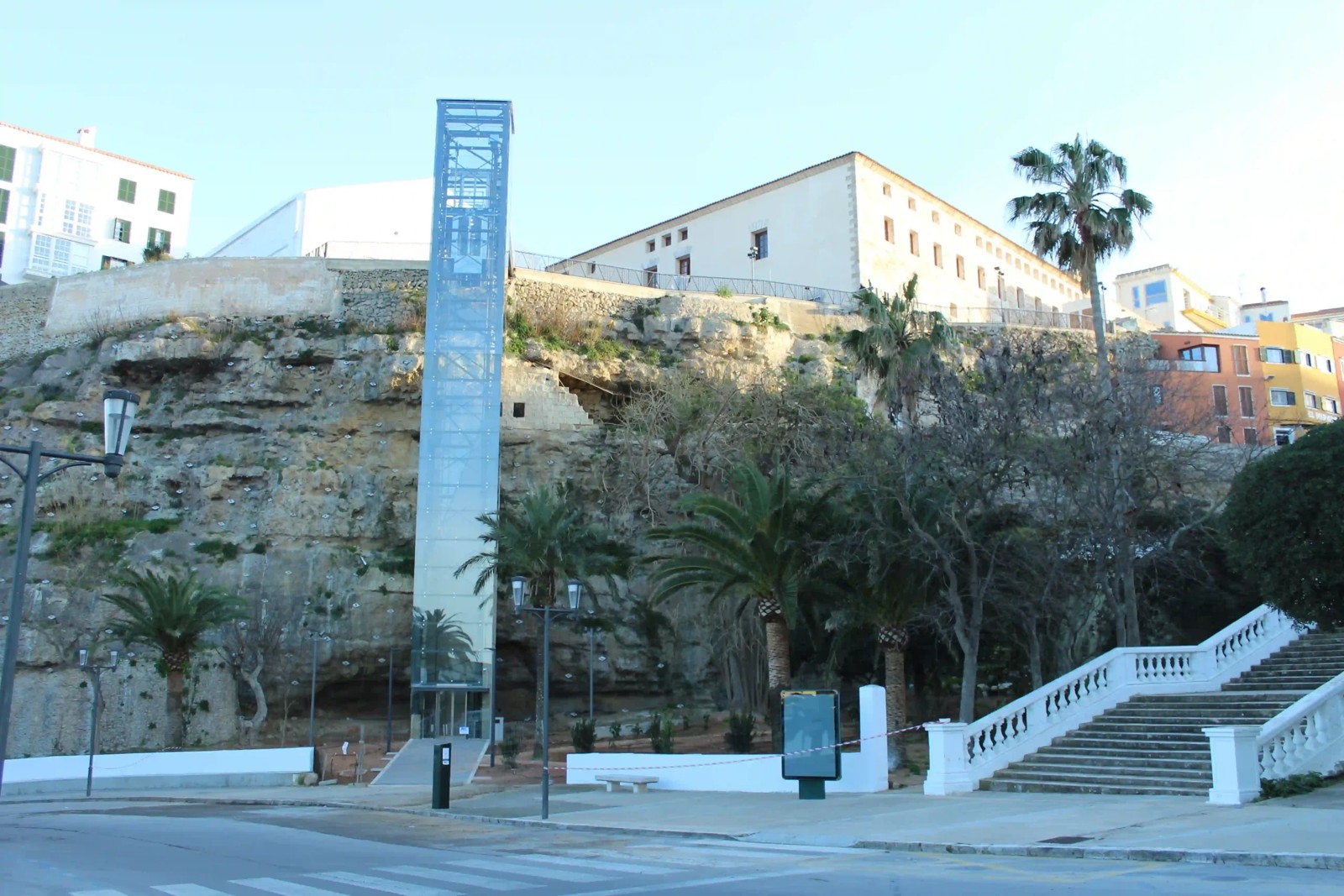 Ascensor panorámico del puerto de Mahón visto desde el muelle, con la torre acristalada adosada al acantilado