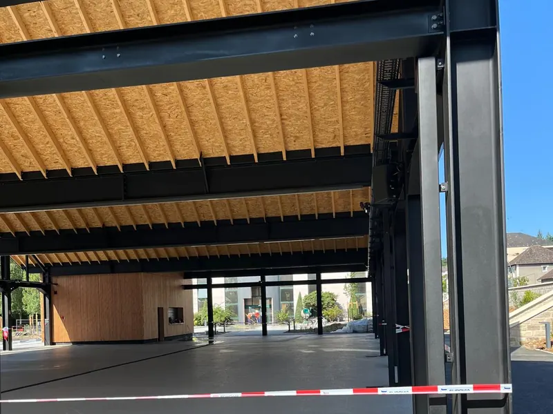 Interior del mercado cubierto terminado: pilares y vigas de acero negro bajo el entablado de madera de la cubierta