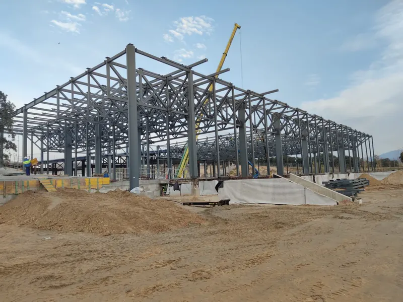 Estructura de acero del pabellón en montaje, con las cerchas de celosía y las gradas todavía en obra