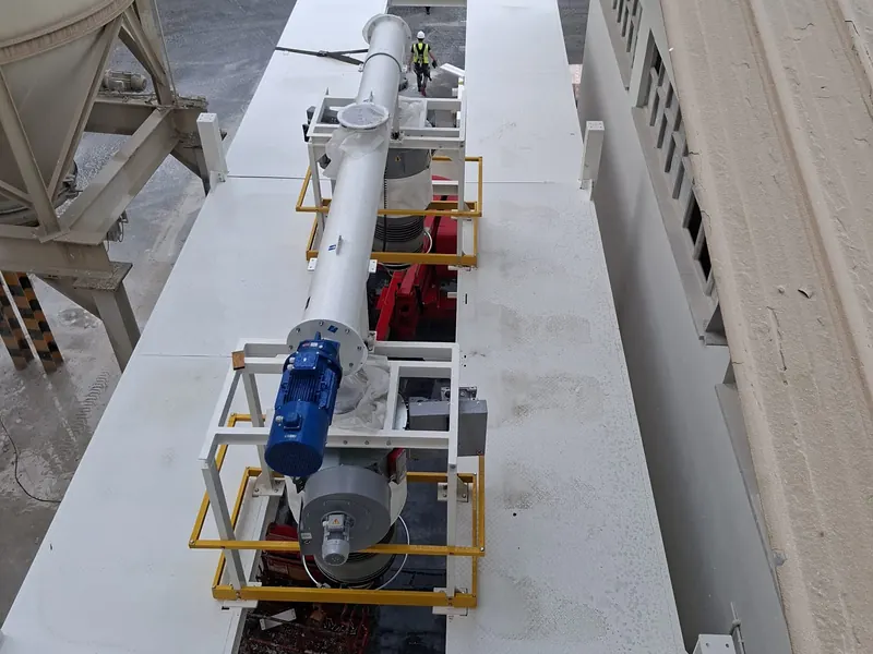 Transportador de tornillo sobre una plataforma de acero blanca, entre silos, en una planta de proceso