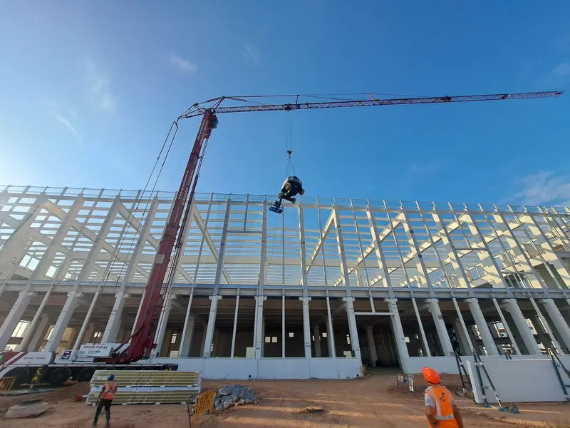 Izado con grúa torre sobre un edificio de gran longitud con estructura de acero blanca