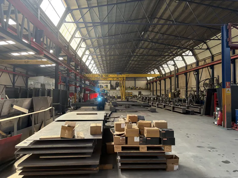 Nave de fabricación de Luvimetal en El Provencio: chapa y material acopiado en primer plano, puestos de soldadura y puente grúa al fondo
